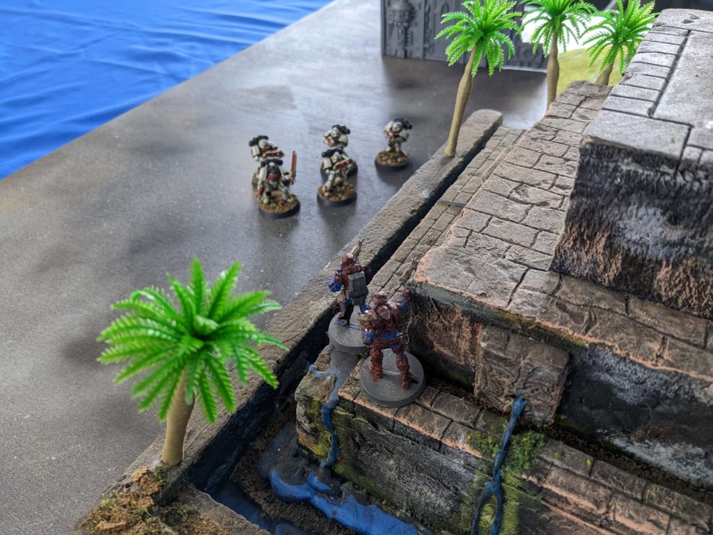 Space Marines face off against two Infinity miniatures on a Mayan pyramid 